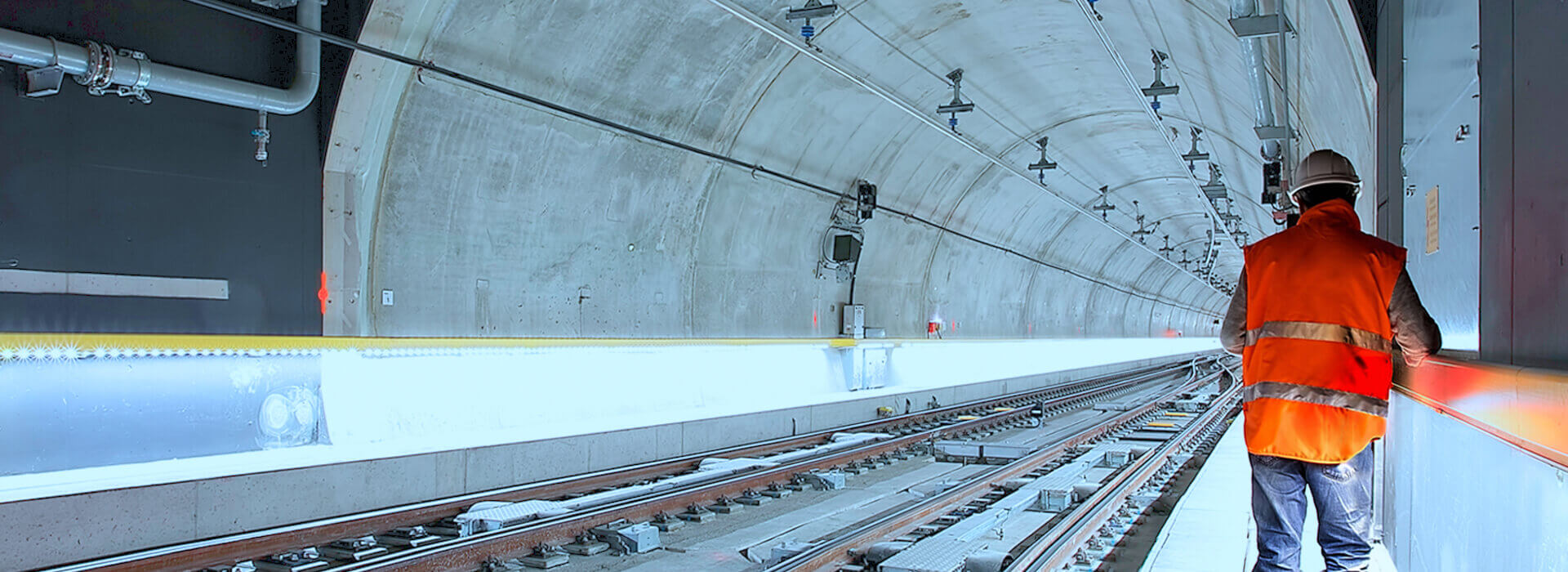 Engenheiro de costas andando em trilhos de metrô com colete sinalizador.