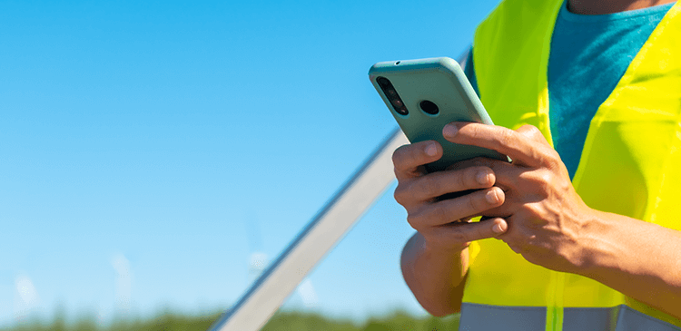 Pessoa vestida com colete refletivo utilizando o celular em canteiro de obras.